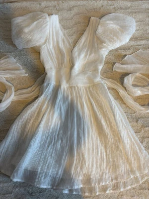 Vit klänning /studentklänning - Säljer en superfin helt vit klänning med puffiga korta ärmar och vacker struktur i tyget. Klänningen har v-ringning, markerad midja och medföljande band som kan knytas. Den är insydd lite vid ryggen så skulle passa som 32 oxå. Köpte den på vinted men den var för stor. 