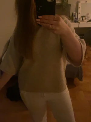 Beige stickad topp med kort ärm - Mysig beige stickad topp med korta ärmar och avslappnad passform. Perfekt att styla med jeans eller kjol för en enkel och clean look. Materialet känns mjukt och toppen har en enkel, tidlös design utan synliga detaljer.