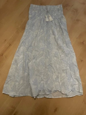 Ljusblå långkjol med mönster - Säljer en ljusblå långkjol med vitt paisleymönster. Den är gjord i ett tunt, luftigt material som passar perfekt till varmare dagar. Säljer den för att den har blivit för liten. 