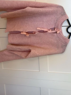 Rosa stickad tröja med rosetter - Supersöt ljusrosa stickad tröja från Gina Tricot med unika rosettknäppningar framtill. Tröjan har rund halsringning, långa ärmar och är gjord i ett mjukt, fluffigt material som känns riktigt cozy.