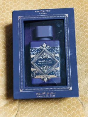 Lattafa Bade'e Al Oud Amethyst parfym - Lattafa Bade'e Al Oud Amethyst är en parfym i en elegant, fyrkantig lila flaska med dekorativa gulddetaljer och orientaliskt mönster. Flaskan kommer i en matchande lila ask med fönster, vilket ger en lyxig känsla. Perfekt för dig som gillar unika och exklusiva dofter.