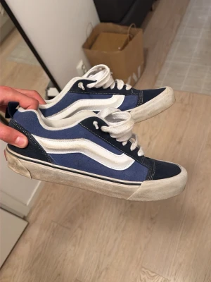 Blåa Vans Old Skool sneakers - Säljer ett par klassiska Vans Old Skool sneakers i blått och vitt. Skorna har den ikoniska vita sidoremsan, vit sula och ovandel i mocka och canvas. Perfekta för en avslappnad streetstil och passar till det mesta. Snygg retrovibe och bekväm passform.