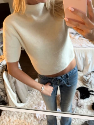 Vit croppad stickad topp - Superfin vit croppad stickad topp med korta ärmar och hög hals. Perfekt att styla med jeans eller kjol för en trendig look. Knappt använd i storlek s från Gina Tricot