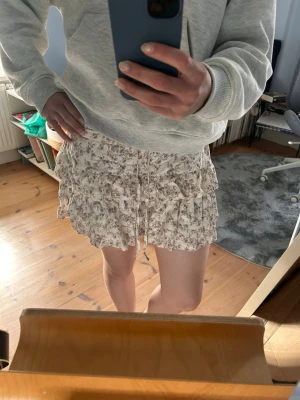 Blommig volangkjol - Supersöt kort kjol med blommigt mönster i beige och lila toner. Ca 35cm från överkant till underkant. 🥰
