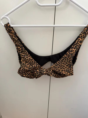 Leopardmönstrad bikiniöverdel från New Beach - Snygg bikiniöverdel från New Beach med leopardmönster i bruna och svarta toner. Modellen har breda axelband och en knutdetalj framtill. Perfekt för strandhäng och sommarens alla bad. Materialet är mjukt och stretchigt syntet.