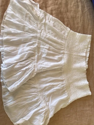 Vita volangshorts med hög midja - Säljer ett en vit kjol. De är tillverkade i ett lätt och luftigt tyg, perfekta för varma dagar.  Kjolen har en feminin och flowy look som passar till många olika stilar.