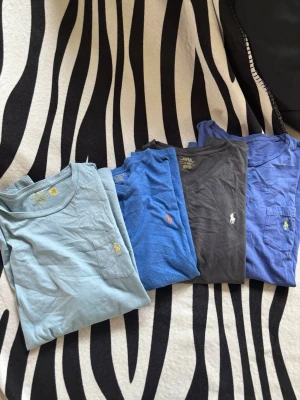 4 pack T-shirts från Polo Ralph Lauren  - Fyra snygga t-shirts från Ralph Lauren i olika blå nyanser. Alla har korta ärmar, rund halsringning och en liten ficka med den klassiska Polo-loggan broderad på bröstet. Perfekta för en clean och avslappnad stil.