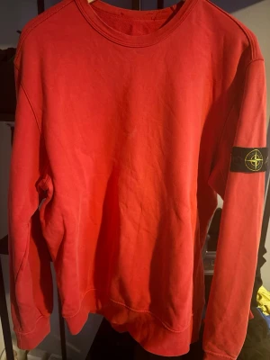 Röd sweatshirt från Stone Island - Röd sweatshirt från Stone Island med klassisk rund hals och ikonisk logotyp-patch på vänster ärm. Tröjan har en avslappnad passform och är tillverkad i mjuk bomull. Perfekt för en streetwear-look.