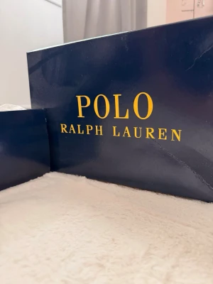 Vita Polo Ralph Lauren sneakers - Snygga vita sneakers från Polo Ralph Lauren med rosa detaljer och klassisk logga på sidan. Skorna har lågt skaft, vita snören och rosa insida samt glitterdetalj på hälen. Perfekta för en trendig och sportig look.