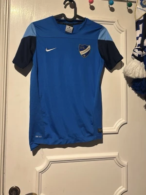 Blå IFK Norrköping matchtröja Nike - Snygg blå matchtröja från Nike med IFK Norrköping-emblem på bröstet. Tröjan har mörkblå och ljusblå detaljer på axlar och ärmar samt vit Nike-logga. Materialet är lätt och andas, perfekt för träning eller match. Stadium-logga på ryggen.