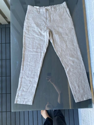 Helt nya Beigebruna linnebyxor med smal passform - Snygga beige linnebyxor med smal passform och klassisk design. Nypris 600kr och säljs mycket billigare då de inte passade för bra, satt lite tight på mig som är 185 och väger 71kg, jag tror det beror på att jag är stor i låren. Helt nya med tagg och allt. De är också lite mörkare, alltså mer åt mockafärg än vit