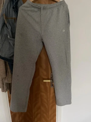 Grå mjukisbyxor  - Säljer ett par klassiska grå mjukisbyxor från Asics med resår i midjan och dragsko. Byxorna har raka ben och sidofickor, perfekta för chill eller träning. Materialet är mjukt och skönt, troligtvis bomull eller bomullsblandning.