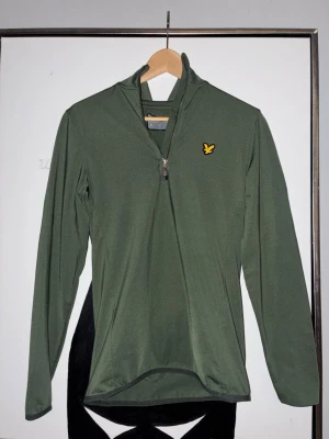 Grön ziptröja från Lyle & Scott - Mörkgrön långärmad ziptröja från Lyle & Scott med halv dragkedja och den klassiska gula loggan på bröstet. Det är en golf tröja som ser stilren ut ute på banan. Ny pris runt 700 kronor mitt pris 499kr. 