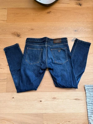 Mörkblå jeans från Armani - Snygga mörkblå jeans från Armani med klassisk femficksdesign och raka ben. Jeansen har en diskret logotyp på bakfickan och läderpatch vid linningen. Materialet är slitstark denim i bomull och passformen är normal.