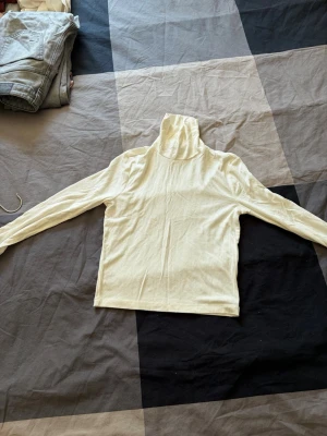 Vit ribbad polotröja - Säljer en stilren vit ribbad polotröja med lång ärm. Tröjan har en hög krage och är tillverkad i ett mjukt, stretchigt material som sitter skönt mot kroppen. Perfekt att bära under jackor eller som den är för en clean look.