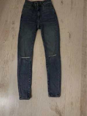 Blåa skinny jeans med slitningar - Säljer ett par mörkblå skinny jeans med hög midja och slitningar vid knäna. 