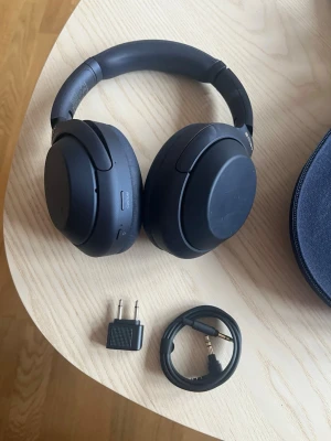Svarta over-ear hörlurar Sony WH-1000XM4 - Snygga svarta over-ear hörlurar från Sony, modell WH-1000XM4. Trådlösa med brusreducering, mjuka öronkuddar och justerbar bygel. Inkluderar flygplansadapter och 3,5 mm ljudkabel. Perfekta för musik, gaming eller resor. Fick dessa i födelsedagspresent men fick också AirPods, blev att jag använde AirPods, så därför säljer jag dessa efter knappt någon användning