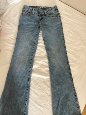 Blå bootcut jeans från 157 - Säljer ett par ljusblå bootcut jeans från 157 med snygga broderade detaljer på bakfickorna. Klassisk femficksmodell med normal midja och bälteshällor. Jeansen är gjorda i denim och har en avslappnad passform med utsvängda ben.