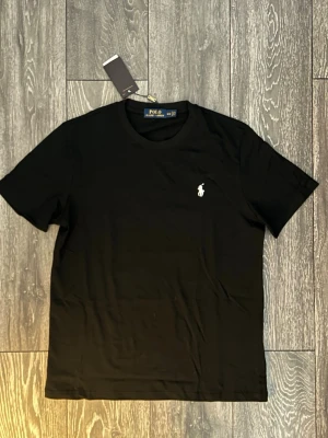 Svart Ralph Lauren T-Shirt - Svart Ralph Lauren T-Shirt helt oanvänd, Perfekt till sommaren ☀️ Men säljer då den var i fel storlek (M) Bara att skriva vid minsta fundering 💭 