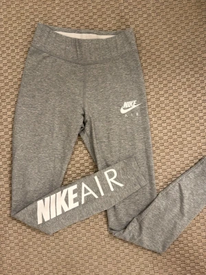 Grå Nike Air leggings - Snygga grå leggings från Nike Air med vit logga på låret och stort tryck längs benet. Stretchigt material som sitter tajt och bekvämt. Perfekta för en sportig look eller till chill-outfiten.