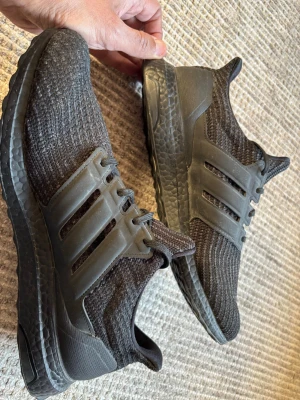 Svarta Adidas Ultraboost DNA sneakers - Säljer ett par helsvarta Adidas Ultraboost sneakers med stickad ovandel i mesh och klassiska tre ränder i plast på sidorna. Skorna har en tjock, responsiv Boost-sula och låg profil. Perfekta för dig som gillar sportig och clean stil. Som ny, endast använd ett fåtal gånger. Ordinarie pris är 2000 kr i Intersport.