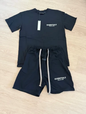 Svart Essentials t-shirt från Fear of God - Svart t-shirt från Fear of God Essentials med vit logga tryckt på bröstet. T-shirten har rund hals och korta ärmar, tillverkad i mjukt material för en avslappnad look.