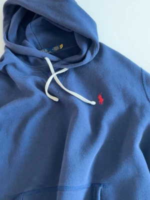 Blå hoodie från Polo Ralph Lauren - Mörkblå hoodie från Polo Ralph Lauren med klassisk röd logga broderad på bröstet. Om de är några frågor så är de bara att ställa