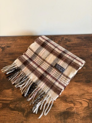 Burberry Halsduk - Vintage Burberrys halsduk i 100% lambswool. Made in England. Klassisk check i mörkare/bruna toner med diskret och tidlös look. Väldigt bra skick med endast mindre tecken på användning. Perfekt för en clean casual/old money stil.