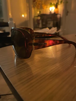 Bruna oversized solglasögon från Prada - Snygga oversized solglasögon från Prada i brun plast med mörka glas. Bågarna har en lätt glansig finish och diskret Prada-logga sidorna