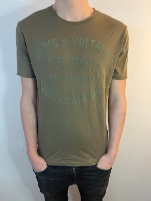 Olivgrön Zadig & Voltaire t-shirt - Snygg olivgrön t-shirt från Zadig & Voltaire med tryck framtill. Tröjan är i toppskick utan några defekter. Tröjan är i storlek xs och sitter slim. Modellen på bilden är 175 och väger 62kg. Hör av dig vid minsta fråga eller fundering! 