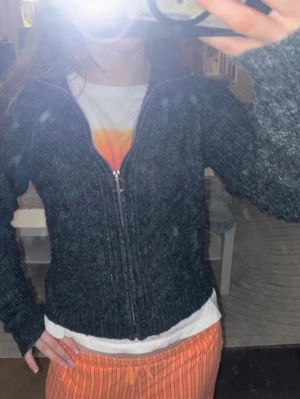 Mörkgrå stickad ziptröja - Mysig mörkgrå stickad tröja med dragkedja framtill och lång ärm. Tröjan har en enkel, klassisk design och passar perfekt till vardags. Ribbstickade detaljer längs ärmar och nederkant ger en snygg finish.😍🔥