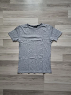 Grå basic t-shirt  - En enkel grå t-shirt med rund hals och korta ärmar. Tillverkad i mjuk bomull för en bekväm känsla. Perfekt till jeans eller shorts och funkar året runt. Klassisk passform och stilren design.