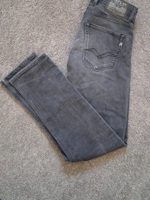 Grå/svarta jeans från Replay - Säljer ett par grå jeans från Replay med rak passform och klassisk femficksdesign. Jeansen har en snygg tvättad look och detaljerade sömmar på bakfickorna. Tillverkade i mjukt denimtyg som ger en skön känsla och stilren vibe.