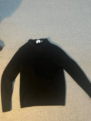 Svart stickad tröja från BläcK - Klassisk svart stickad tröja från BläcK med rund halsringning och ribbade muddar vid ärmslut och nederkant. Enkel och stilren design som passar till det mesta. Perfekt basplagg för garderoben.