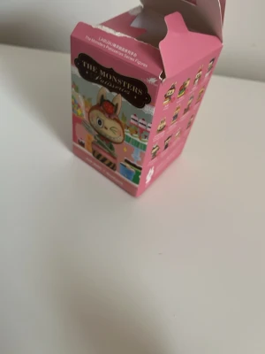 Pop Mart The Monsters figur med låda - Säljer en Pop Mart The Monsters samlarfigur med original rosa låda.  Figur: Tutti frutti meringue cake.  Säljer: lådan,kortet och Labubu. Obs: lådan är öppnad! Påsen den kom i följer ej med. 
