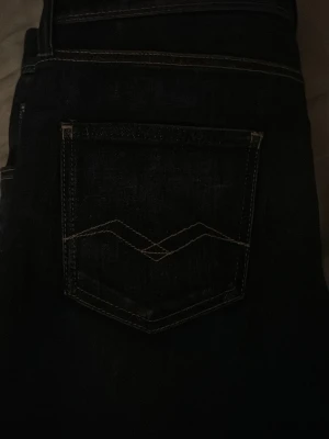 Mörkblå jeans med kontrastsöm - Snygga mörkblå jeans med klassisk femficksdesign och vit kontrastsöm på bakfickan. Jeansen har raka ben och är tillverkade i ett slitstarkt denimtyg. Perfekta för en avslappnad och trendig look.