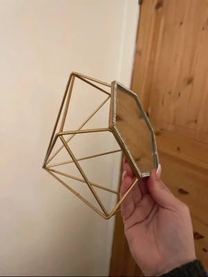 spegel med guldram - Säljer en unik sminkspegel med sexkantig form och tunn guldfärgad metallram. Spegeln har dekorativa små stenar runt kanten som ger en lyxig känsla. Perfekt som detalj på sminkbordet eller i badrummet. Rengörs innan den skickas 