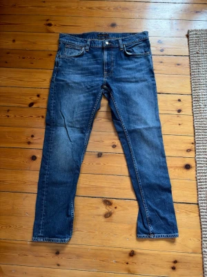 Mörkblå jeans från Nudie Jeans - Säljer ett par klassiska mörkblå jeans från Nudie. Storleken är W32 och L30. Jeansen har en defekt mellan benen som ej syns när man har dem på sig och är lätt att fixa för den som kan! Om du har fler frågor så är det bara att höra av dig!