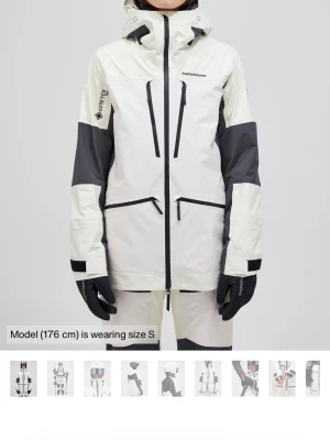 Peak Performance - søger!! - Snygg vit och grå skaljacka från Peak Performance med svarta detaljer, vattentätt GORE-TEX-material, justerbar huva och flera dragkedjeförsedda fickor. Perfekt för skidåkning eller andra vinteraktiviteter. Jackan har en modern passform och hög krage.