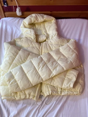 Ljusgul pufferjacka från Zara - Säljer en ljusgul pufferjacka från Zara med luva. Har använt den ca 1 gång. Den är i storlek XXL. Man kan spänna ut och in nere vid dragkedjan som på bilden 🧥