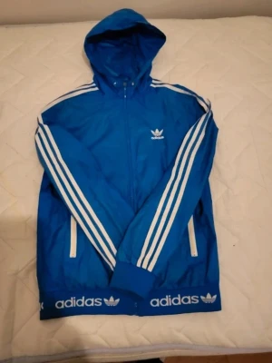 Blå Adidas vindjacka med huva - Fin jacka från Adidas, hål under armen som lätt går att sy igen storlek s