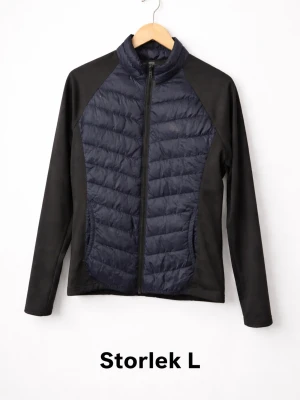 Svart hybrid pufferjacka Lager 157 - Snygg svart hybrid pufferjacka från Lager 157 i storlek L. Jackan har quiltad front och rygg i mörkblått, släta svarta ärmar och sidor samt hel dragkedja framtill. Perfekt för kalla dagar med sin lätta och värmande design.