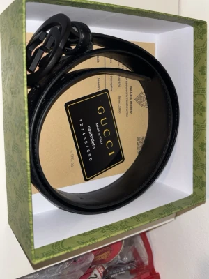 Gucci bälte  - Snyggt svart bälte från Gucci i äkta läder med klassiskt GG-spänne i matt svart metall. Bältet har präglade GG-loggor längs remmen och justerbara hål för perfekt passform. Perfekt accessoar för att lyfta vilken outfit som helst.