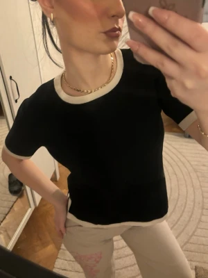 Zara topp❤️ - Snygg svart topp med beige kant vid halsringning, ärmslut och nederkant. Modellen är enkel och rak med korta ärmar, perfekt för en stilren look. Materialet känns mjukt och bekvämt mot huden.