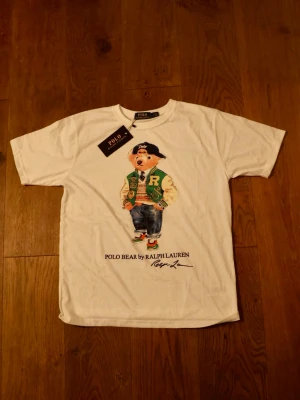 Vit Polo Bear t-shirt från Ralph Lauren - Skickar snabbt📦 | Ny med tags👔 | Size L | Vit t-shirt från Polo Ralph Lauren med ikoniskt Polo Bear-tryck framtill. T-shirten har rund hals och korta ärmar. Tillverkad i mjuk bomull och har en avslappnad passform. Perfekt för dig som gillar klassisk streetstyle med en twist.