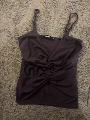 Mörklila ribbad linnetopp Bik Bok - Trendig mörklila ribbad linnetopp från Bik Bok med smala axelband och snygg twistad detalj framtill. Toppen har v-ringning och croppad passform, perfekt att styla till jeans eller kjol.