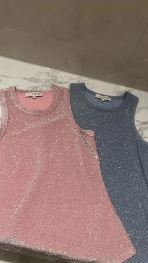 Glittrig linnetopp från A VIEW - Supersnygg glittrig linnetopp från A VIEW i  blått. Toppen är ärmlös med rund halsringning och har en glittrig finish som verkligen sticker ut. Perfekt för dig som vill ha något extra till outfiten.