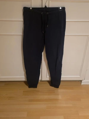 Mörkblå mjukisbyxor - Mörkblå mjukisbyxor med dragsko i midjan och resår vid bensluten. Byxorna har en bakficka.