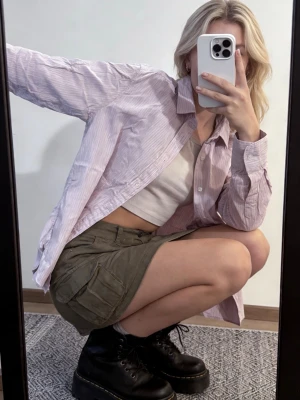 Ljusrosa randig skjorta - Säljer en ljusrosa skjorta med tunna vita ränder. Skjortan har klassisk krage, knäppning framtill och långa ärmar. Passformen är lite loose och materialet känns som bomull. Perfekt att styla över ett linne eller t-shirt.