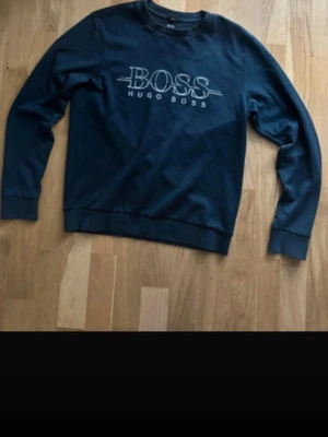 Mörkblå sweatshirt från Hugo Boss - Snygg mörkblå sweatshirt från Hugo Boss med stort vitt logotryck på bröstet. Tröjan har rund halsringning, långa ärmar och ribbade muddar vid ärmslut och nederkant. Perfekt för en avslappnad och stilren look.